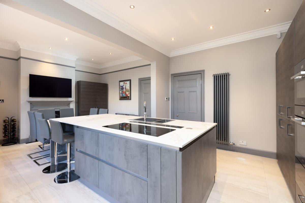 A spacious kitchen renovation with large fitted cabinetry and integrated appliances. A kitchen island sits in the centre of the space, with a dining area.