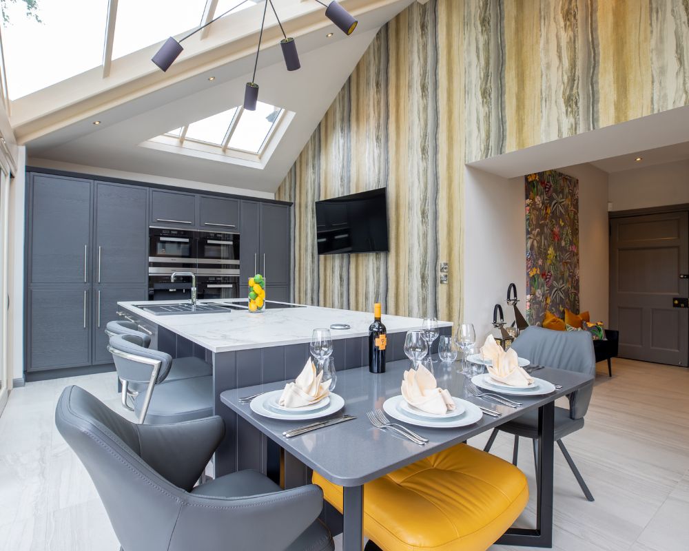 An Orangery kitchen renovation with a fitted kitchen cabinet with integrated appliances. A large kitchen island with an extended dining area with a mounted TV for entertainment.