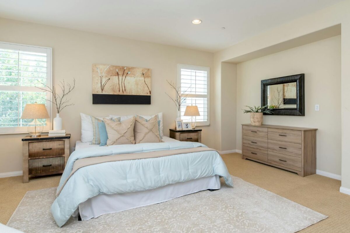 A spacious bedroom renovation with a large bed and storage furniture for folded clothes. Two bedside lamps sit on top of a bedside cabinet.