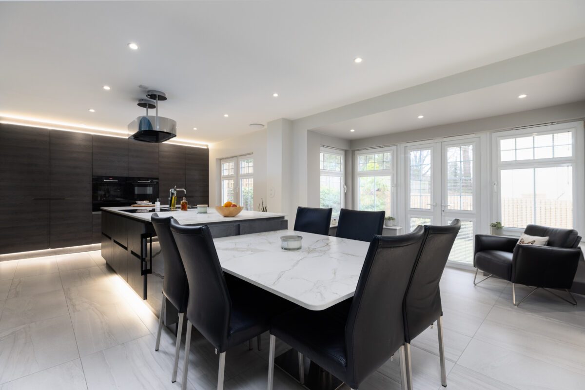A spacious, modern kitchen featuring floor-to-ceiling cabinetry with integrated appliances. The kitchen space includes a central island and a dining area.