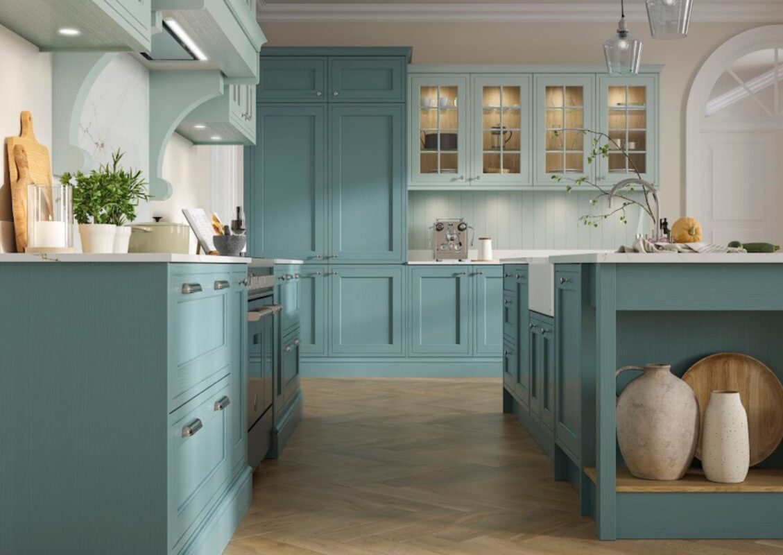 A modern kitchen renovation with a central island with a built-in farmhouse sink. The kitchen includes bespoke teal blue cabinetry complemented by chrome handles and fixtures.